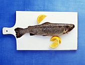 A trout with lemon wedges on white kitchen board