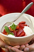 Two hands holding a bowl of vanilla ice cream & strawberries