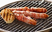 Bacon-wrapped sausages and slice of baguette on barbecue
