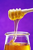 Honey running from a honey dipper into a jar