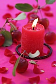 Burning candle surrounded by crab apples and flower petals