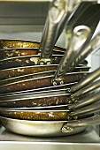 A pile of frying pans in a commercial kitchen
