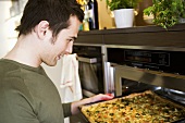 Young man putting vegetable pizza into oven (on baking tray)