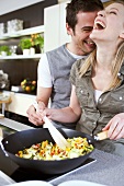 Young couple cooking vegetables in wok, laughing