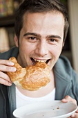 Junger Mann beisst in ein Croissant