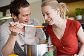Young couple tasting tomato sauce from wooden spoon