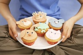 Child holding plate of muffins with animal faces