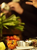 Still life with vegetables, person in background preparing food