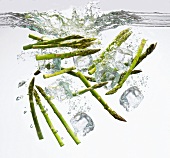 Green asparagus spears and ice cubes falling into water