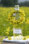 Eine Flasche Rapsöl mit Blütenkränzchen