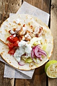 Chicken souvlaki with a vegetable salad and a yogurt dressing on flat bread