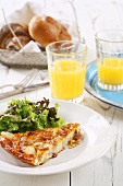 A slice of frittata with a mixed salad and a glass of orange juice