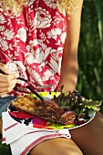 A woman holding a plate of grilled spare ribs