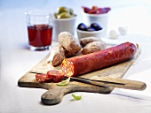 Chorizo on a chopping board with red wine, basil, olives and dried tomatoes