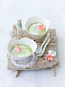 Two bowls of sorrel soup with geranium flowers on wooden board