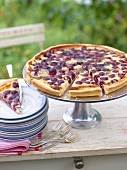 Cherry tart with poppy seeds, partly sliced, on cake stand outside