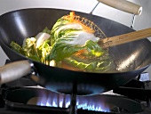 Gemüse wird in einem Wok auf Gasflamme angebraten
