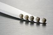 Five white peppercorns on a knife blade