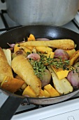 Root vegetables in a frying pan on a gas cooker