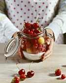 Woman holding a preserving jar full of mixed fruit & sugar