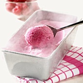 Melting raspberry ice cream in ice cream container with spoon