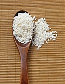 Sticky rice on and beside a wooden spoon on a bamboo mat