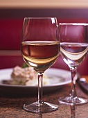 Ein Glas Weißwein, ein Glas Wasser, Gericht im Hintergrund