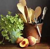 Kitchen utensils in a clay pot with coriander and peaches
