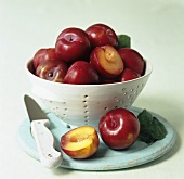 Red plums in a colander and on a wooden board with knife