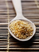 Raw cane sugar in a wooden spoon on a bamboo mat