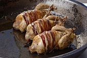 Frying three barded quails in a frying pan