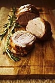 Roast lamb, cut into pieces, with rosemary on wooden board