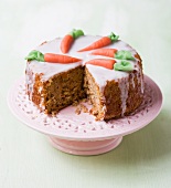 Iced carrot cake with a piece removed, on cake stand