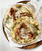 Two pizzas topped with coppa, cheese and pesto