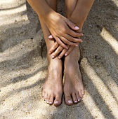Frau sitzt im Sand (Nahaufnahme Füsse und Hände)