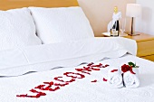 Begrüssungsschrift "Welcome", rote Rosen und Handtücher auf Bett im Hotelzimmer