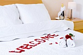 Red roses, handtowels and the word 'Welcome' written on a bed in a hotel room