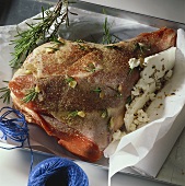 Raw leg of lamb studded with rosemary & garlic on baking parchment
