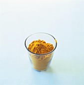 Ground turmeric in a glass, white background