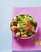 Tomaten-Mozzarella-Spieße auf grünem Salat, Schinken, Melone