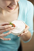Young woman dipping a strawberry in yoghurt
