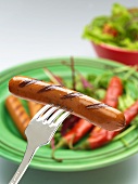 A grilled sausage speared on a fork