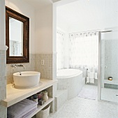 Waschtisch und Wandspiegel in einer Nische neben runder Badewanne unter Fenstereckfront