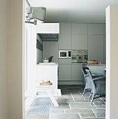 Blick in eine moderne Küche mit grauen Korbstühlen und Steinfliesen