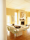 Heavy, white dining table and simple shell chairs in yellow dining room with open fireplace