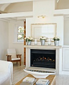 Lit fire under flowers in zinc buckets on stone mantelpiece and gilt-framed picture