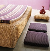 Wicker lounger with mattress, two floor cushions and glass carafe on small wicker table