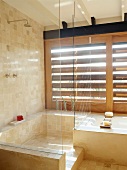 Transparente Duschkabine neben Badewanne vor Fensterläden aus Holz im mediterranem Bad