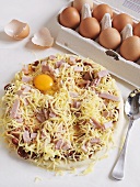 An unbaked pizza topped with ham, cheese and egg