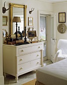 weiße Schlafzimmerkommode mit darüberhängendem goldgerahmten Spiegel